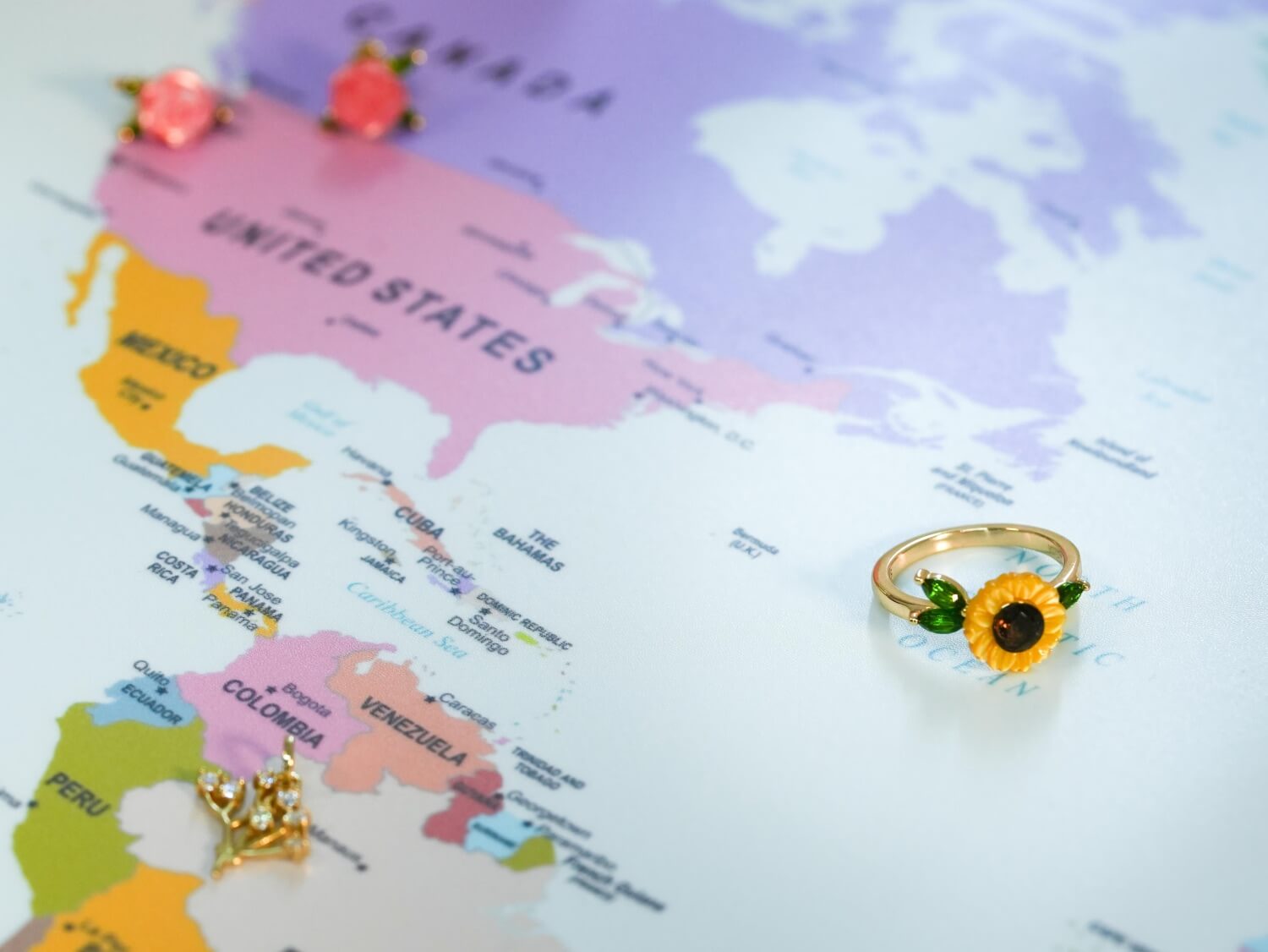 Carved Sunflower Ring and Baby's Breath Charm on a world map, with our Carved Rose Stud Earrings set in the background.